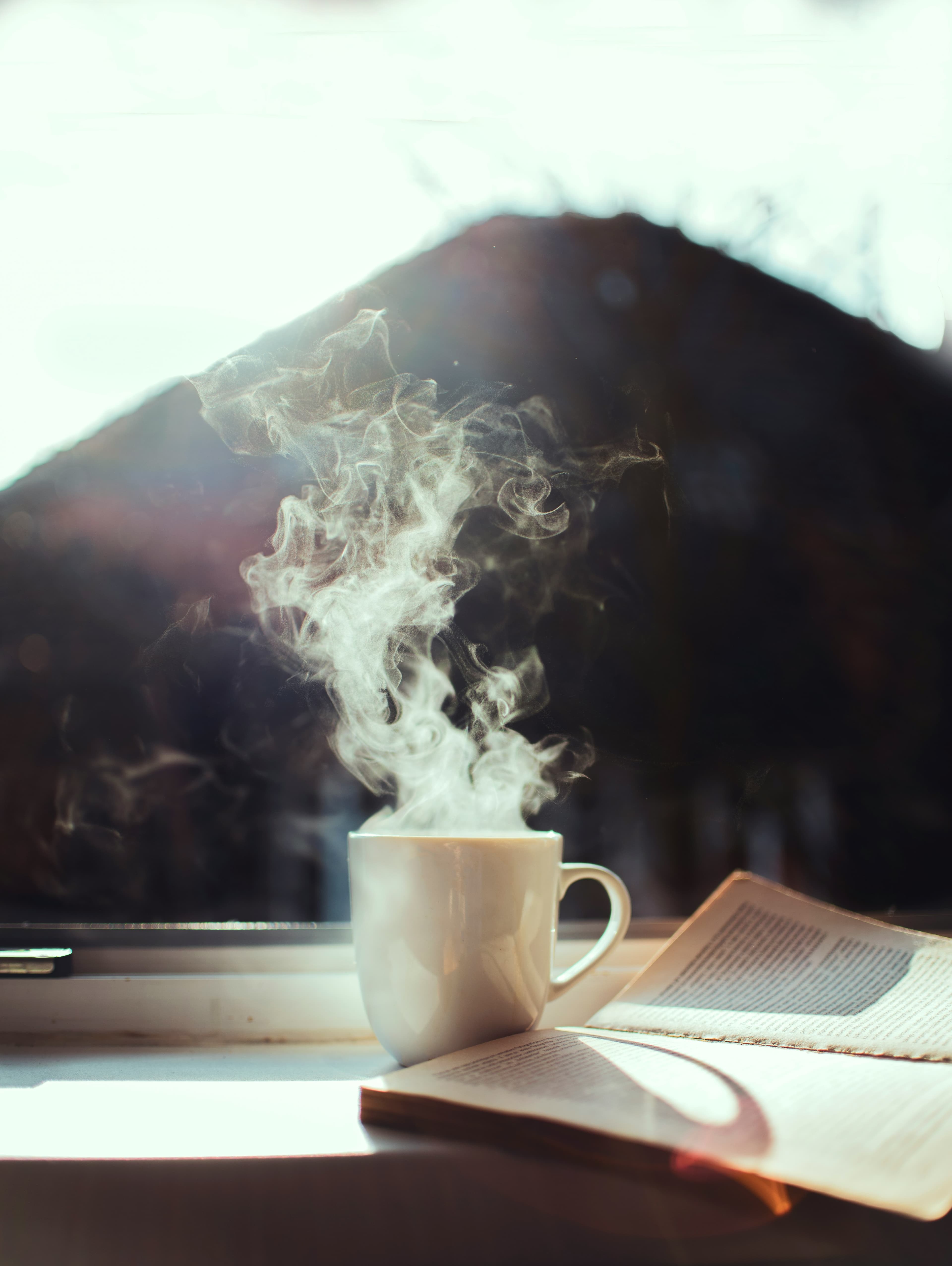 Pencere kenarında buğu tüten bir fincan kahve ve açık bir kitap — Almanca öğrenmenin sabah ritüeli